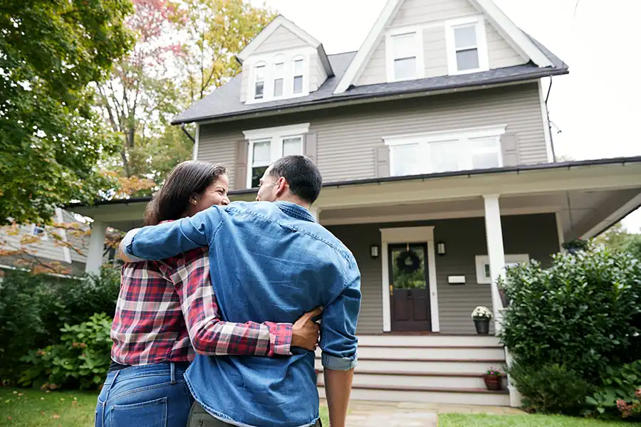 A couple stands arm in arm looking at their home, symbolizing the dream of true homeownership free from perpetual property taxes.